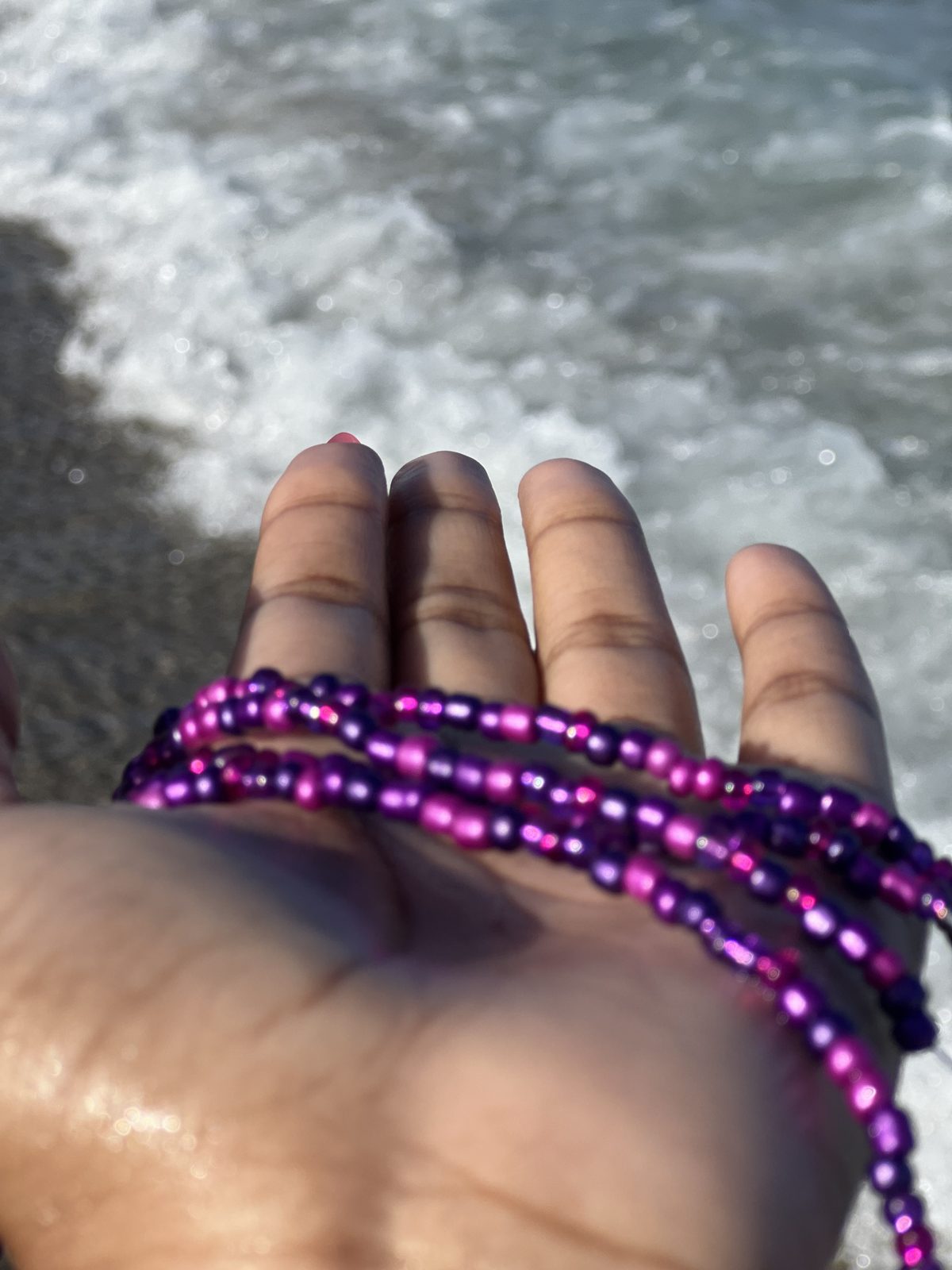 Purple and pink waist beads Zayviana made, held in her hand at the beach