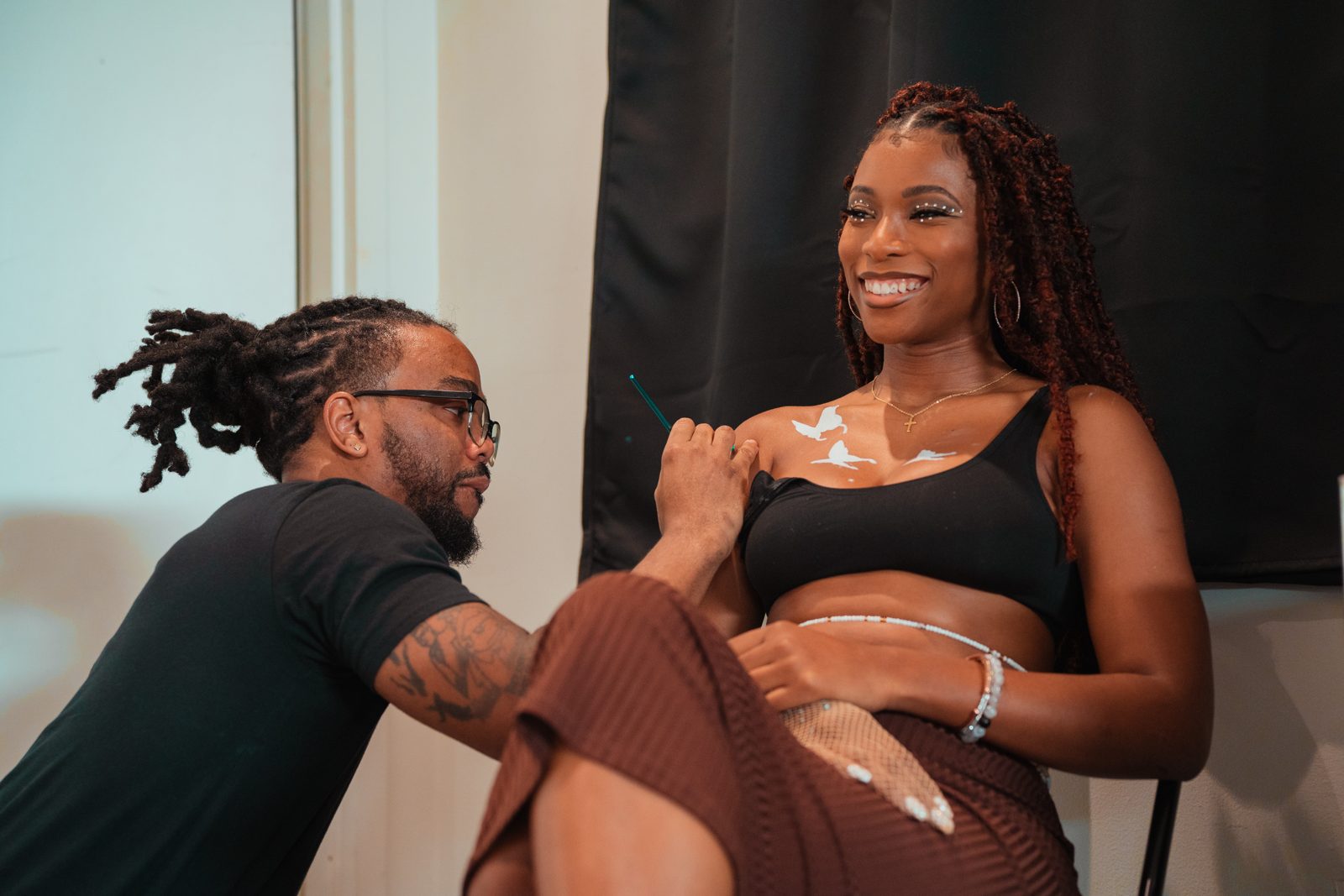 Zayviana smiling while an artist paints a design on her shoulder before a show